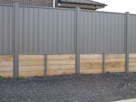 Stepped Colorbond fencing panels installed cleanly on top of a concrete sleeper retaining wall.